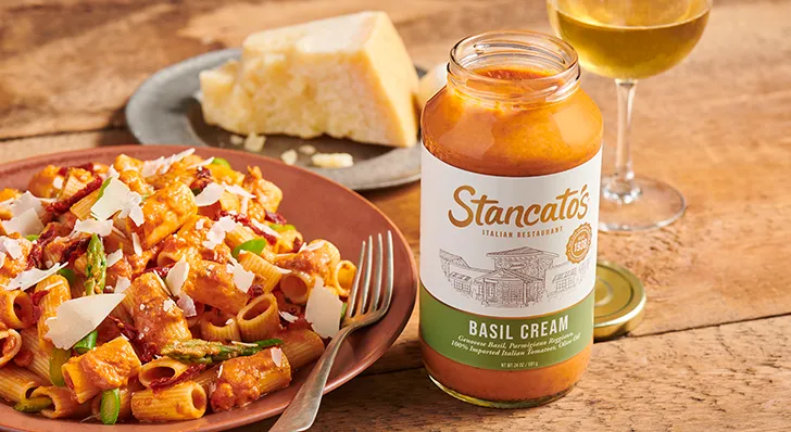 A jar of basil cream pasta sits next to a plate of rigatoni