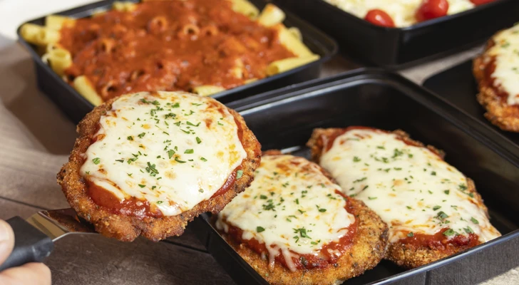 A person serves themself a piece of chicken parmigiana from a catering table